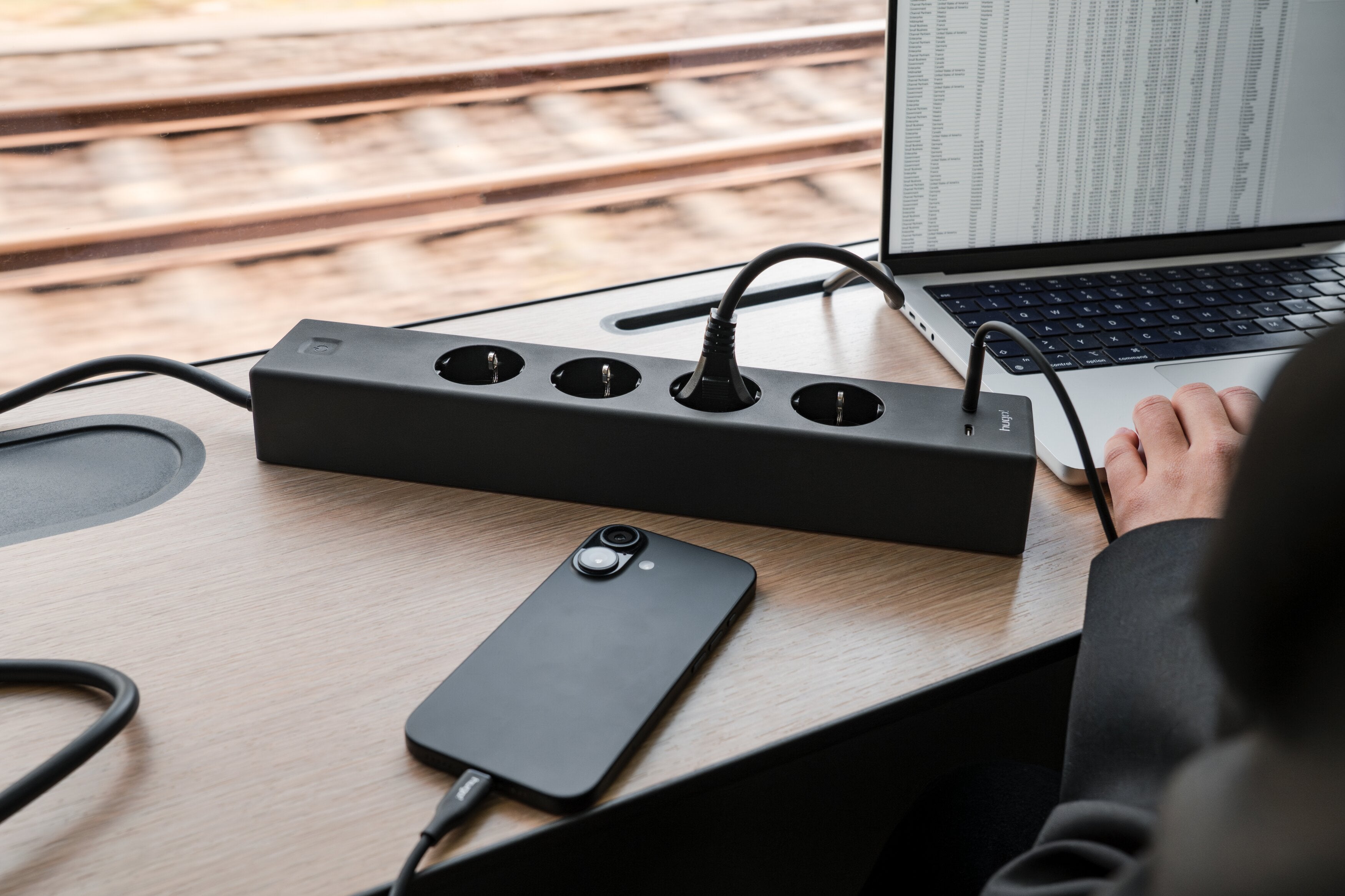 hugo! SOCKET in deep black mit angeschlossenem Laptop und Smartphone im Zug.