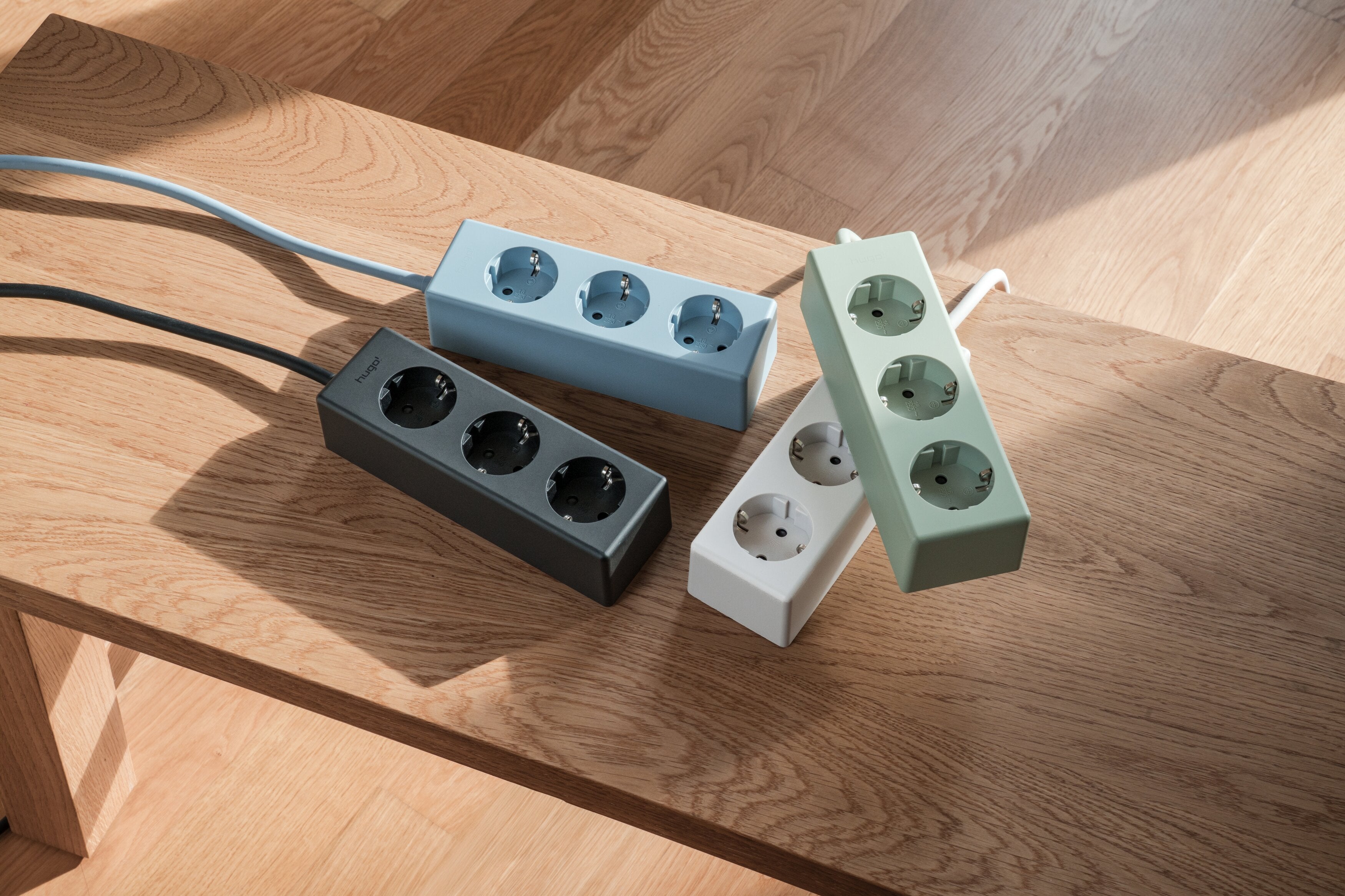Vier hugo! MAGNETIC Steckdosenleisten in verschiedenen Farben auf einem Holztisch.