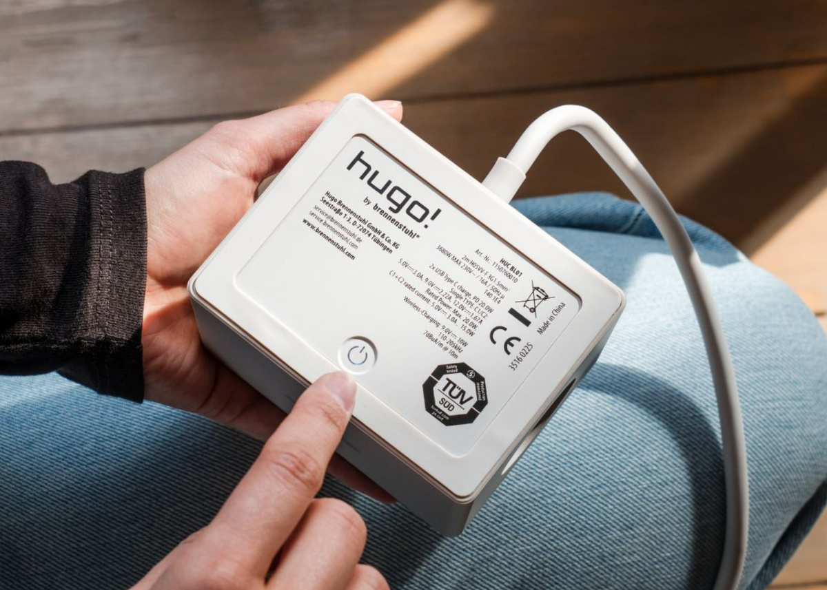 hugo! ONE Steckdosenwürfel in white mit Power-Taste in der Hand.