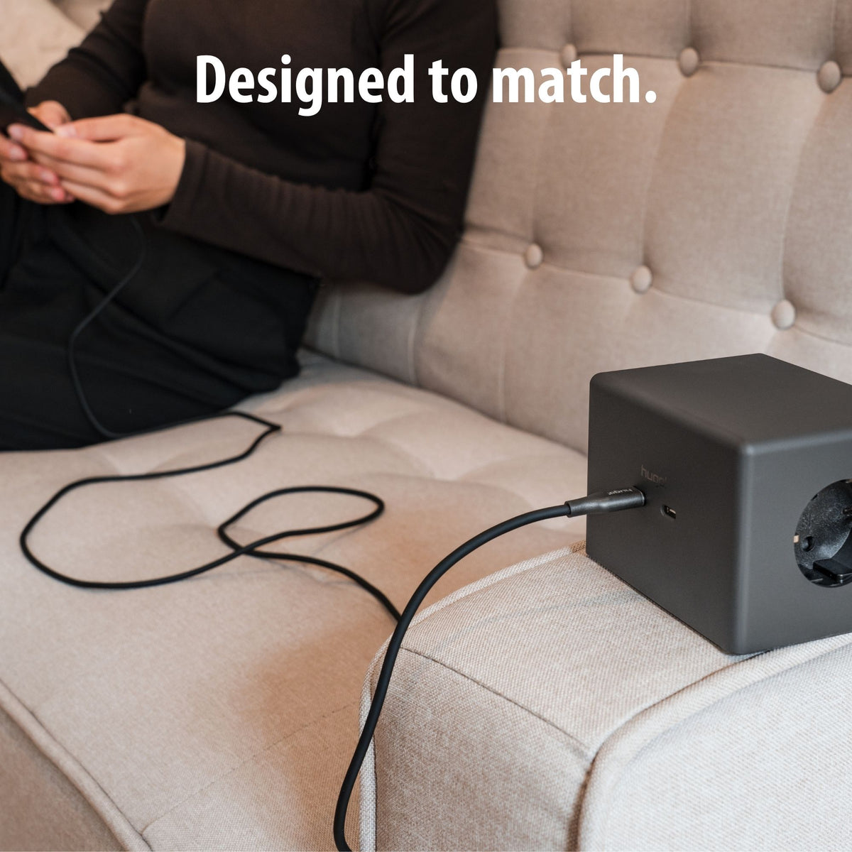 Schwarzes hugo! CABLE verbindet ein Smartphone mit dem hugo! ONE am Sofa.