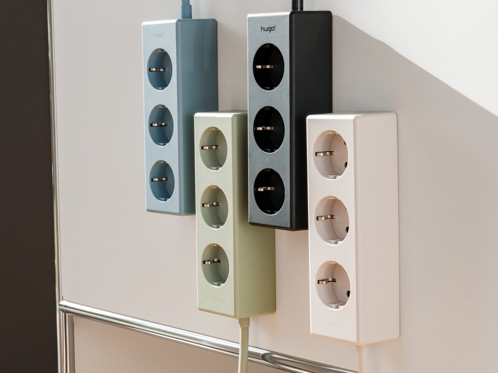„Vier hugo! MAGNETIC Steckdosenleisten in verschiedenen Farben an einer Wand.
