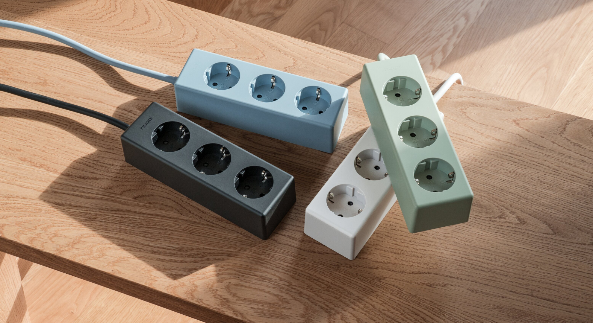 Vier hugo! MAGNETIC Steckdosenleisten in deep black, ice blue, mint green und cream white auf einer Holzbank