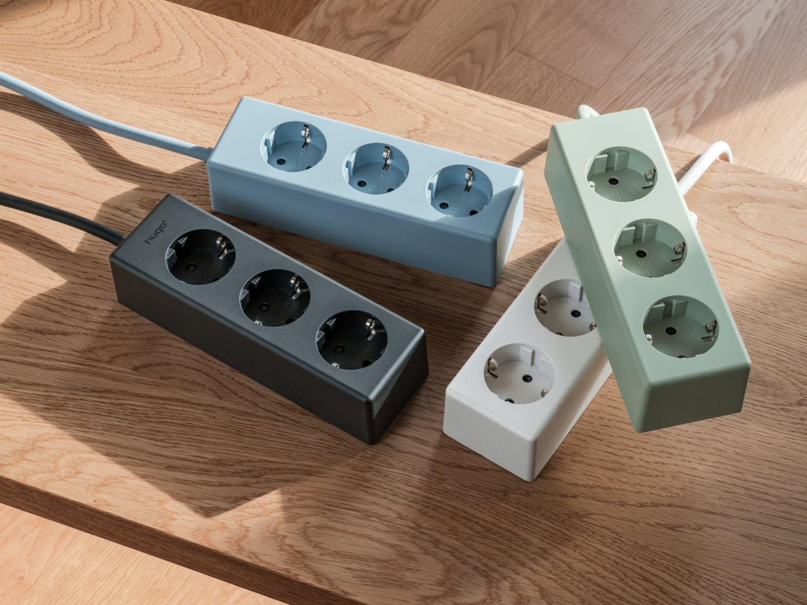 Vier hugo! MAGNETIC Steckdosenleisten in deep black, ice blue, mint green und cream white auf einer Holzbank