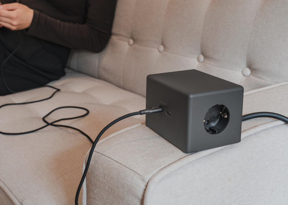 hugo! ONE in deep black mit angeschlossenem USB-C-Kabel auf einer Sofa-Armlehne.