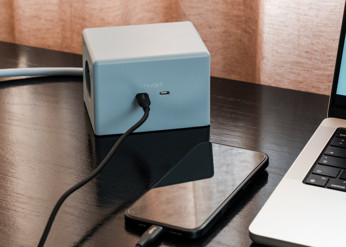 hugo! ONE in ice blue mit eingestecktem USB C-Kabel neben Smartphone und Laptop