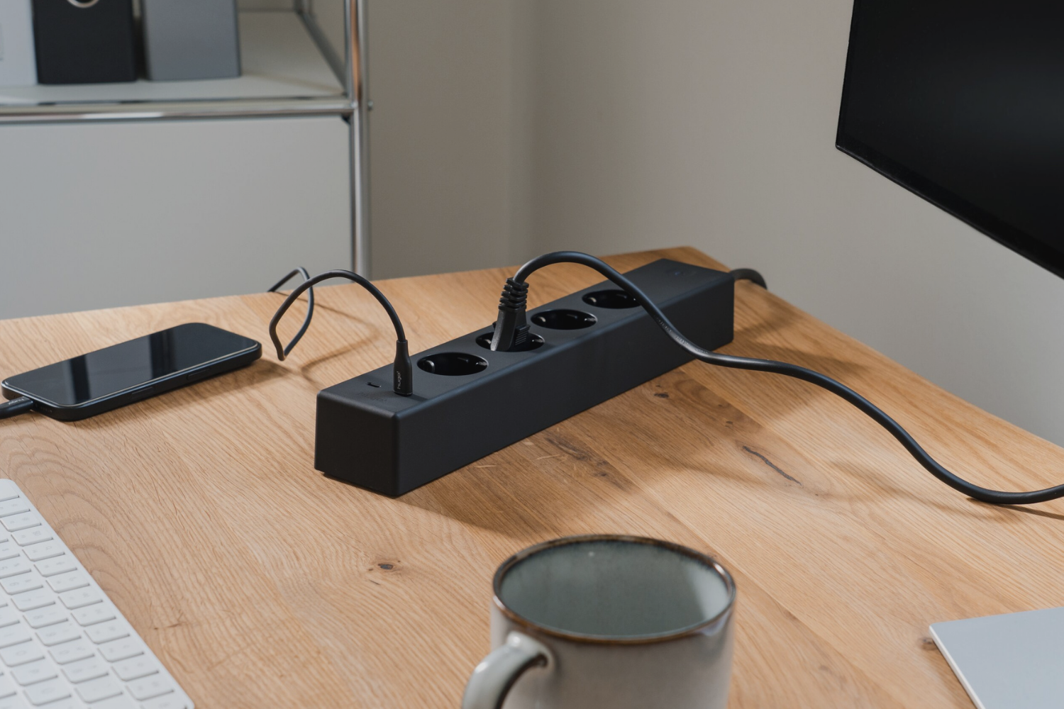 hugo! SOCKET in deep black mit eingesteckten Kabeln auf einem Schreibtisch.